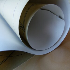 Puede incluir: Una hoja de papel blanco enrollada con un respaldo de papel marr&oacute;n. El papel tiene un patr&oacute;n de cuadr&iacute;cula impreso.