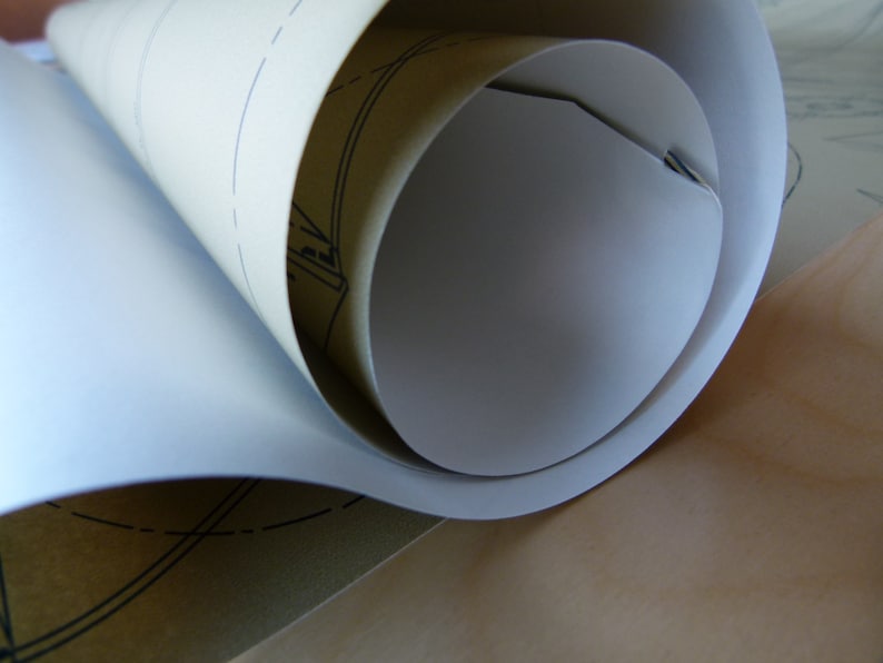 Puede incluir: Una hoja de papel blanco enrollada con un respaldo de papel marr&oacute;n. El papel tiene un patr&oacute;n de cuadr&iacute;cula impreso.