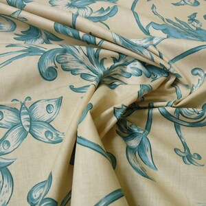 May include: A beige fabric with a blue floral and butterfly pattern. The fabric is folded and draped, showing the design.