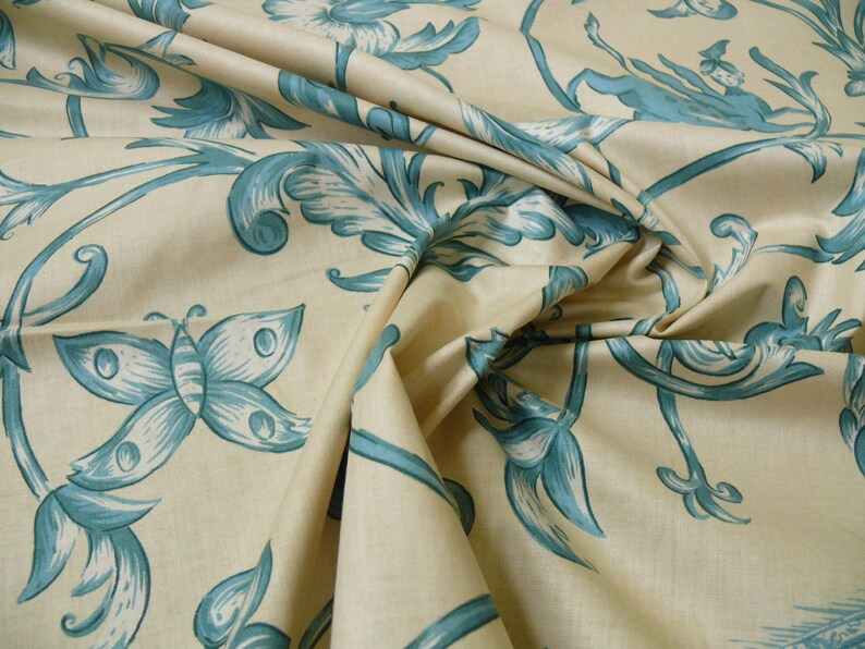 May include: A beige fabric with a blue floral and butterfly pattern. The fabric is folded and draped, showing the design.