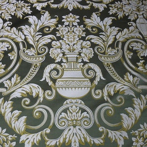 Pu&ograve; includere: Un tessuto verde con un motivo floreale bianco e oro. Il motivo presenta un disegno ripetitivo di foglie stilizzate, fiori e un vaso.