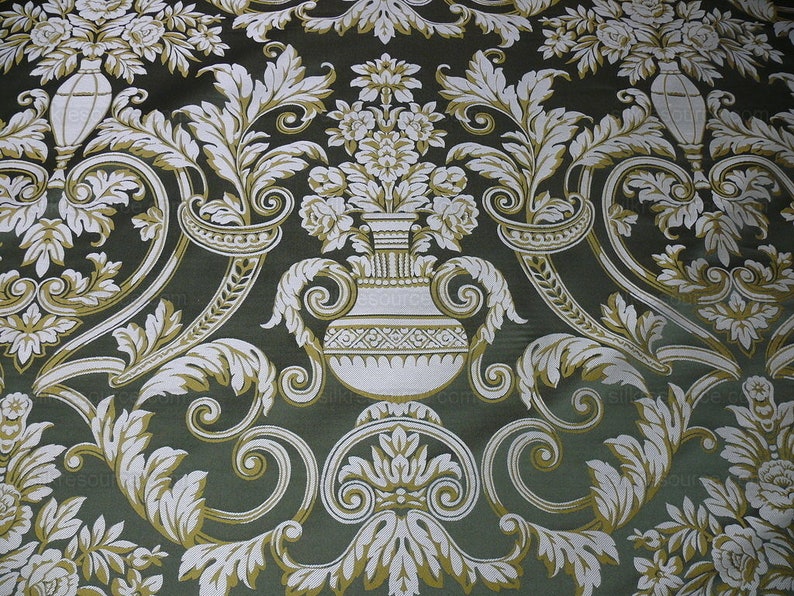 Pu&ograve; includere: Un tessuto verde con un motivo floreale bianco e oro. Il motivo presenta un disegno ripetitivo di foglie stilizzate, fiori e un vaso.
