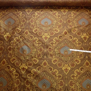 May include: Brown fabric with a gold and blue damask pattern. The fabric has a subtle sheen and a luxurious feel.