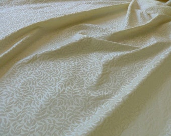 May include: A white fabric with a subtle, embossed leaf pattern. The fabric has a soft, textured feel and a slightly off-white color.