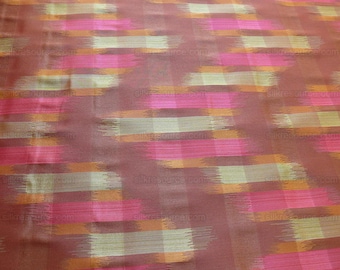 Puede incluir: Primer plano de una tela con un patrón ikat marrón, rosa y dorado. La tela tiene un brillo sutil y una textura suave.