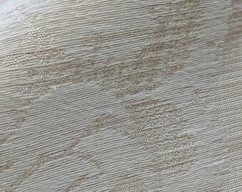 May include: Close-up of a cream-colored fabric with a subtle embossed floral pattern. The fabric has a slightly textured surface.