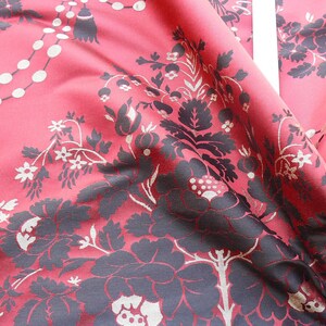 May include: Red fabric with a black floral pattern. The fabric has a subtle sheen and a textured surface.