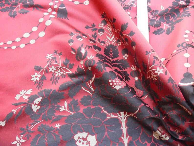 May include: Red fabric with a black floral pattern. The fabric has a subtle sheen and a textured surface.