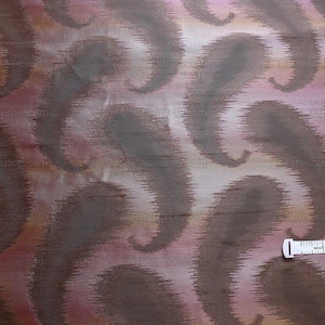 May include: Close-up of a fabric with a paisley pattern in shades of brown, pink, and orange. A white measuring tape is partially visible at the bottom of the image.