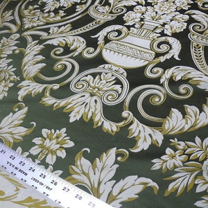 Pu&ograve; includere: Tessuto verde con un motivo floreale bianco e oro. Il motivo presenta un disegno ripetitivo di fiori stilizzati, foglie e un vaso con fiori.