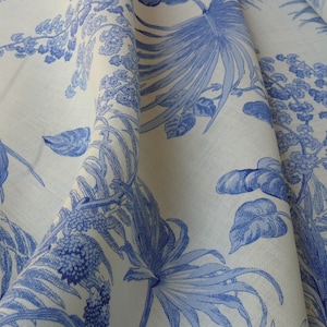 May include: White fabric with a blue floral pattern featuring palm leaves and small blue flowers. The fabric is folded and draped.
