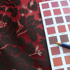 May include: A color chart with a variety of red, brown, and orange shades. The chart is labeled with color codes, such as "0ac610", "0ac614", and "0ac616". A blue pencil with white dots is lying on top of the chart.