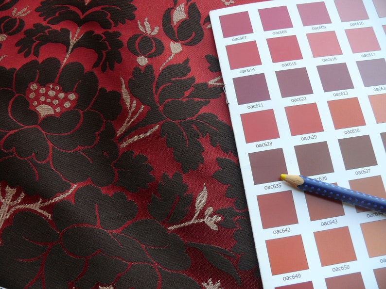 May include: A color chart with a variety of red, brown, and orange shades. The chart is labeled with color codes, such as "0ac610", "0ac614", and "0ac616". A blue pencil with white dots is lying on top of the chart.