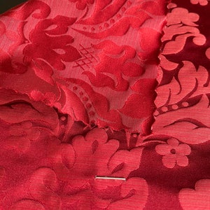 Puede incluir: Tela de damasco roja con un patrón floral. La tela está doblada por la mitad, mostrando el patrón en ambos lados.