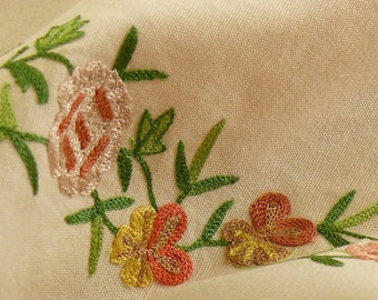 May include: Close-up of embroidered fabric with a floral design. The fabric is a light beige color and the flowers are pink, orange, yellow, and green.