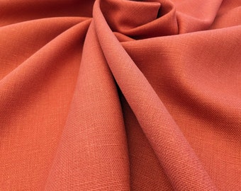 May include: Close-up of a rust-colored fabric with a textured weave. The fabric is folded and draped, showing its soft, drapey texture.