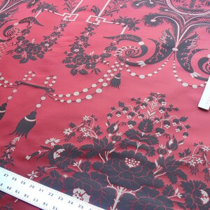 May include: Red fabric with a black and white floral pattern. The fabric has a repeating pattern of flowers, leaves, and beads. The fabric is a damask weave.