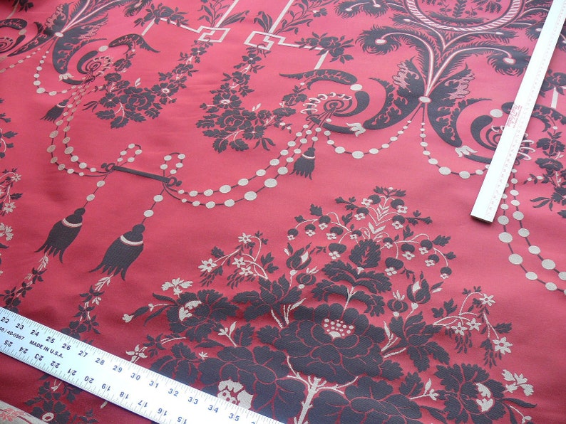 May include: Red fabric with a black and white floral pattern. The fabric has a repeating pattern of flowers, leaves, and beads. The fabric is a damask weave.