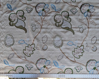 May include: White fabric with a floral embroidery pattern in shades of green, blue, and pink. The design features stylised leaves and flowers.