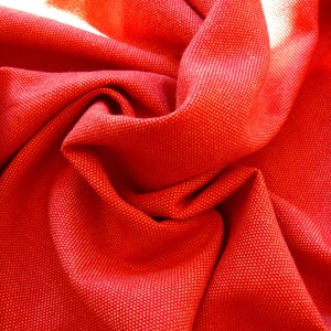 Pode incluir: Tecido vermelho com superfície texturizada. O tecido está dobrado e drapeado, criando um visual suave e fluido.