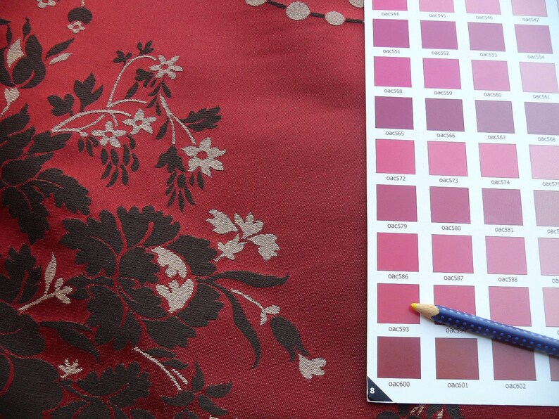 May include: A close-up of a red fabric with a floral pattern in black and white. A color chart with a pencil is on the right side of the image. The color chart has a variety of pink and red shades.