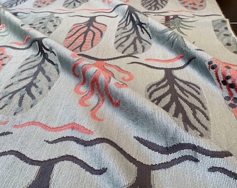 May include: A light blue fabric featuring a repeating pattern of grey and coral-coloured stylized trees and leaves. The textile is folded, revealing its texture and design. The theme is inspired by nature.