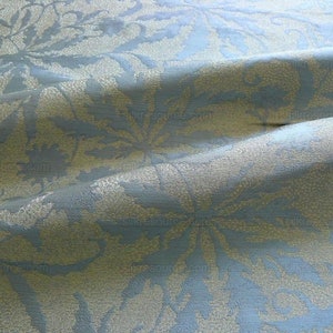 May include: A close-up of a blue fabric with a subtle, embossed pattern of light gold leaves. The fabric has a soft, textured feel.