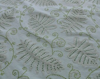 May include: White fabric with a green embroidered design of leaves and vines. The fabric has a textured, raised surface.