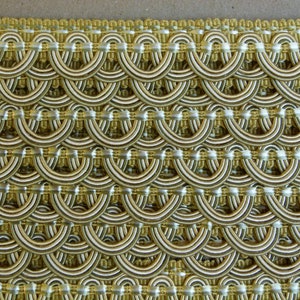 May include: Gold and ivory trim with a repeating pattern of rounded arches. The trim is made of woven fabric and has a subtle sheen.