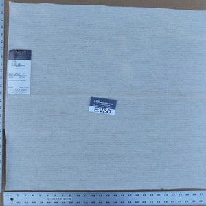 May include: A close-up of a light gray fabric swatch with a white woven texture. The fabric is labeled "Tajik Fabric" and "EV30".