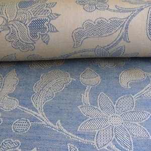 May include: Close-up of a blue and white patterned fabric with a floral design. The fabric has a textured weave and a subtle sheen.