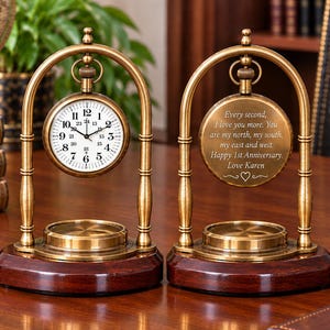 Puede incluir: Dos relojes de escritorio de latón con marcos arqueados y bases de madera oscura. Un reloj presenta una esfera blanca con números negros, mientras que el otro muestra un mensaje grabado: Every second, I love you more. You are my north, my south, my east and west. Happy 1st Anniversary. Love Karen.