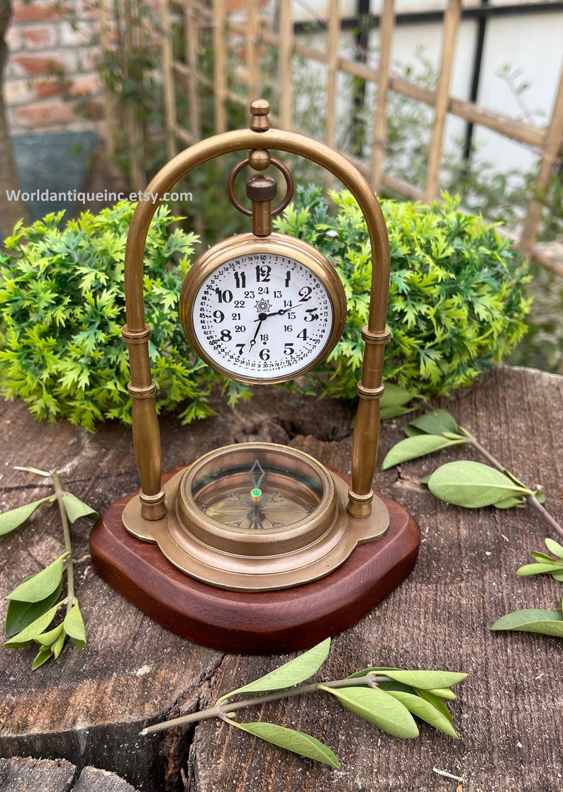 May include: A brass pocket watch with a compass on a wooden base. The watch face has black Roman numerals and a white background. The compass has a green needle and a white background.