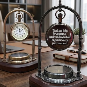 May include: Two desk clocks with dark wood bases and metal arched frames. One clock features a white face with black numerals. The other clock displays the text: Thank you John for 40 years of service and dedication. Congratulations on your retirement!