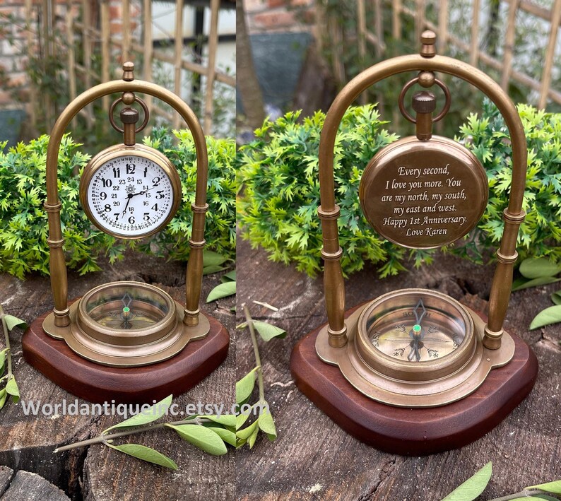 May include: A brass compass and pocket watch on a stand with a wooden base. The watch face has Roman numerals and the compass has a green needle. The watch is engraved with the text "Every second, I love you more. You are my north, my south, my east and west. Happy 1st Anniversary. Love Karen."