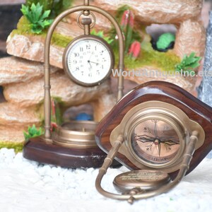 May include: A brass compass and pocket watch on wooden stands. The compass has a white face with black markings and a red needle. The pocket watch has a white face with black Roman numeral markings and black hands. The stands are made of dark wood with a brass trim.