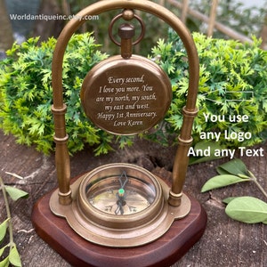May include: A brass compass with a wooden base and a brass stand. The compass face has a green jewel in the centre. The compass is engraved with the text "Every second, I love you more. You are my north, my south, my east and west. Happy 1st Anniversary. Love Karen".