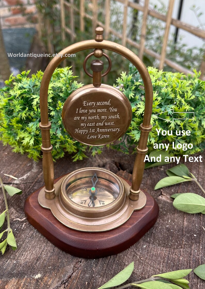 May include: A brass compass with a wooden base and a brass stand. The compass face has a green jewel in the centre. The compass is engraved with the text "Every second, I love you more. You are my north, my south, my east and west. Happy 1st Anniversary. Love Karen".
