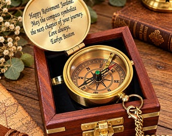 May include: A brass compass with a hinged lid featuring the engraved text: Happy Retirement Jardine. May the compass symbolize the next chapter of your journey. Love always, Earlyn Boston. The compass rests inside a dark wooden box with a gold latch.
