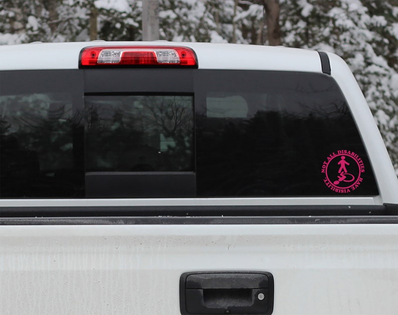 May include: A white pickup truck with a pink sticker on the back window. The sticker says "Not All Disabilities Are Visible" and has a symbol of a person in a wheelchair.
