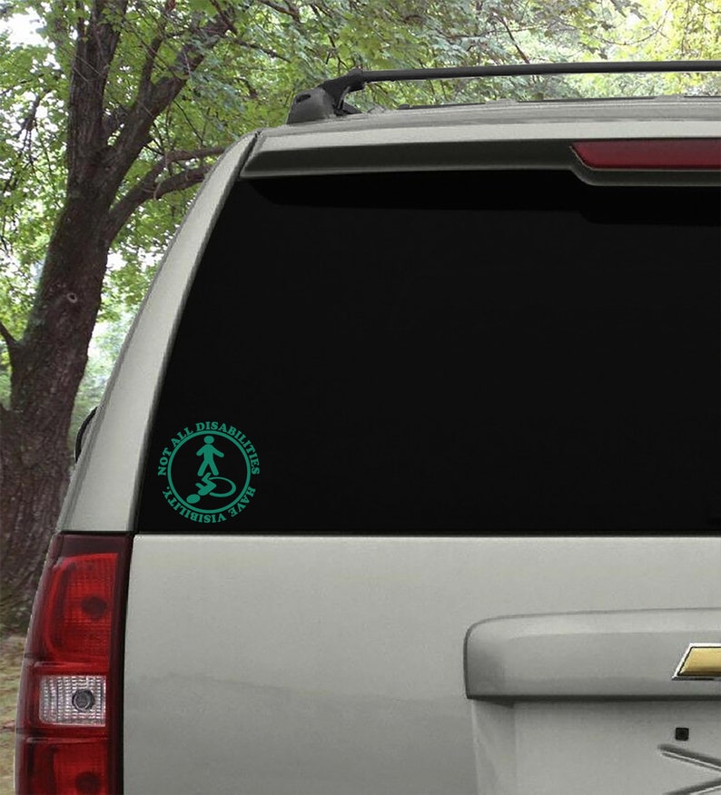 May include: A teal blue sticker on the back of a silver car. The sticker is a circle with the text "NOT ALL DISABILITIES ARE VISIBLE" and a stylized image of a person standing and a person in a wheelchair.