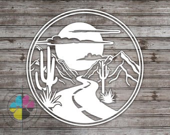 May include: A white circular cutout design featuring a desert landscape with a winding road, mountains, saguaro cacti, and a large sun in the background. The graphic is enclosed within a double-lined circular border, creating a clean, layered silhouette.
