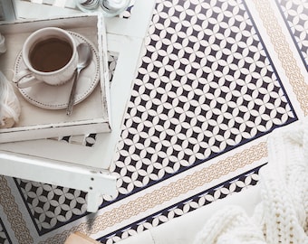 May include: A white knitted blanket with a cable knit pattern is draped over a black and white patterned floor tile. A cup of coffee and a book are on a white tray in the upper left corner of the image. The floor tile has a gold and blue border. The text "CHINUA FLOORING" is visible in the lower left corner of the image.