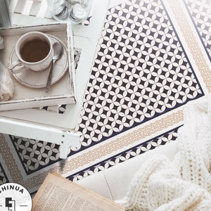 Könnte beinhalten: Eine weiße Strickdecke mit einem Zopfmuster liegt auf einer schwarz-weißen gemusterten Bodenfliese. Eine Tasse Kaffee und ein Buch befinden sich auf einem weißen Tablett in der oberen linken Ecke des Bildes. Die Bodenfliese hat einen goldenen und blauen Rand. Der Text "CHINUA FLOORING" ist in der unteren linken Ecke des Bildes sichtbar.