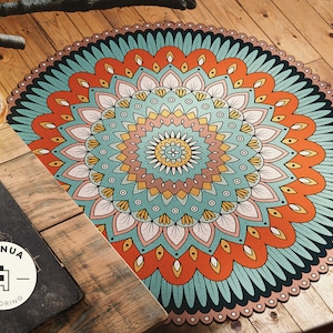 May include: A round, colorful mandala rug with a teal, orange, and pink design. The rug has a circular pattern with intricate details and a black border.