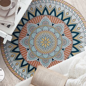 May include: A round, colorful mandala rug with a blue, yellow, orange, and pink design. The rug is on a wooden floor with a white blanket and a book on top of it.