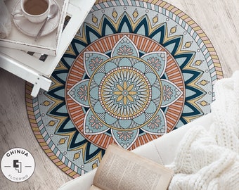 Puede incluir: Una alfombra redonda de mandala colorida con un diseño azul, amarillo, naranja y rosa. La alfombra está sobre un suelo de madera con una manta blanca y un libro encima.