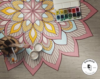 May include: A colorful mandala rug with pink, yellow, and blue hues. The rug has a detailed design with intricate patterns. There are paintbrushes and paint jars on the rug, along with a watercolor palette.