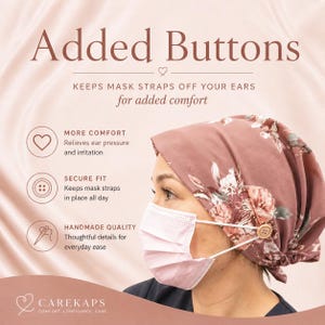 Op de afbeelding: Een roze bloemen scrub cap met knopen om maskerriemen vast te houden, voor comfort en een veilige pasvorm. De tekst luidt "Added Buttons" en "Keeps mask straps off your ears for added comfort."