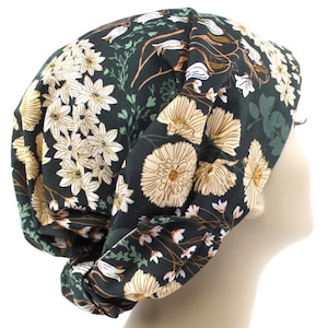 May include: A dark green hat with a floral pattern of white and beige flowers, green leaves and stems. The hat is made of soft fabric and is designed to be worn on the head.